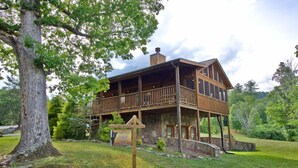 Een houten chalet met een balkon, omgeven door bomen en een stenen fundering.