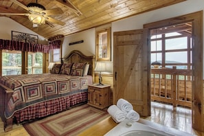 Um quarto aconchegante com uma cama grande, cabeceira de madeira, mesa de cabeceira, abajur e vista para o exterior através de uma porta.