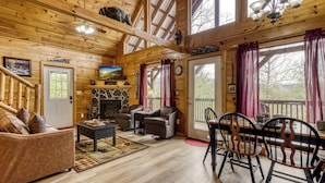 Interior acogedor de una cabaña de troncos con chimenea, muebles de cuero y ventanas amplias.