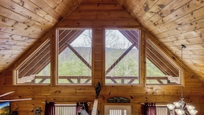 Un interior de madera con techo inclinado, ventanas grandes y una escalera de madera.