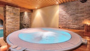 A hot tub in a room with wooden ceiling and stone walls.