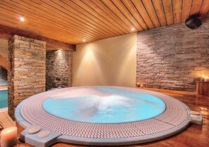A hot tub in a room with wooden ceiling and stone walls.