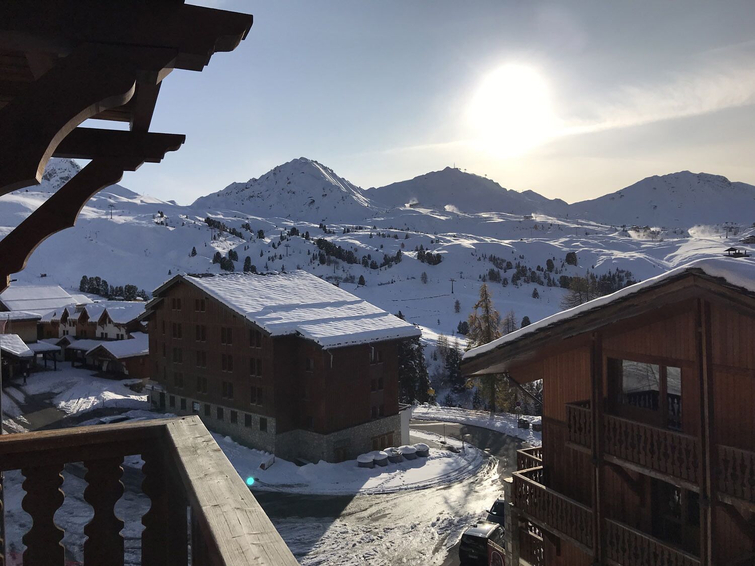 Un village de montagne enneigé, avec des bâtiments en bois et une vue dégagée sur le soleil.