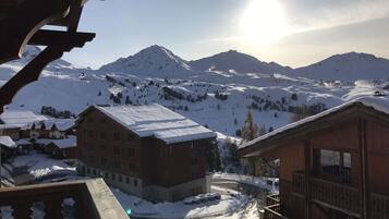 Un village de montagne enneigé, avec des bâtiments en bois et une vue dégagée sur le soleil.