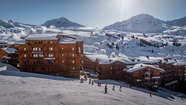 A ski resort with wooden buildings, ski slopes, and a mountainous backdrop.
