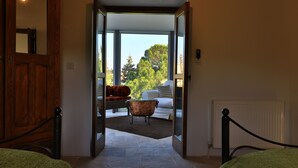An open doorway leading to a balcony with a view of trees and a white chair. - Estia Anogaia Cottage (Ora)