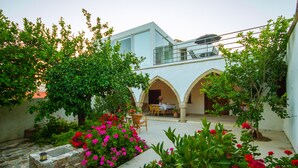A courtyard with a stone fountain, lush greenery, and a dining area with outdoor seating. - Estia Anogaia Cottage (Ora)