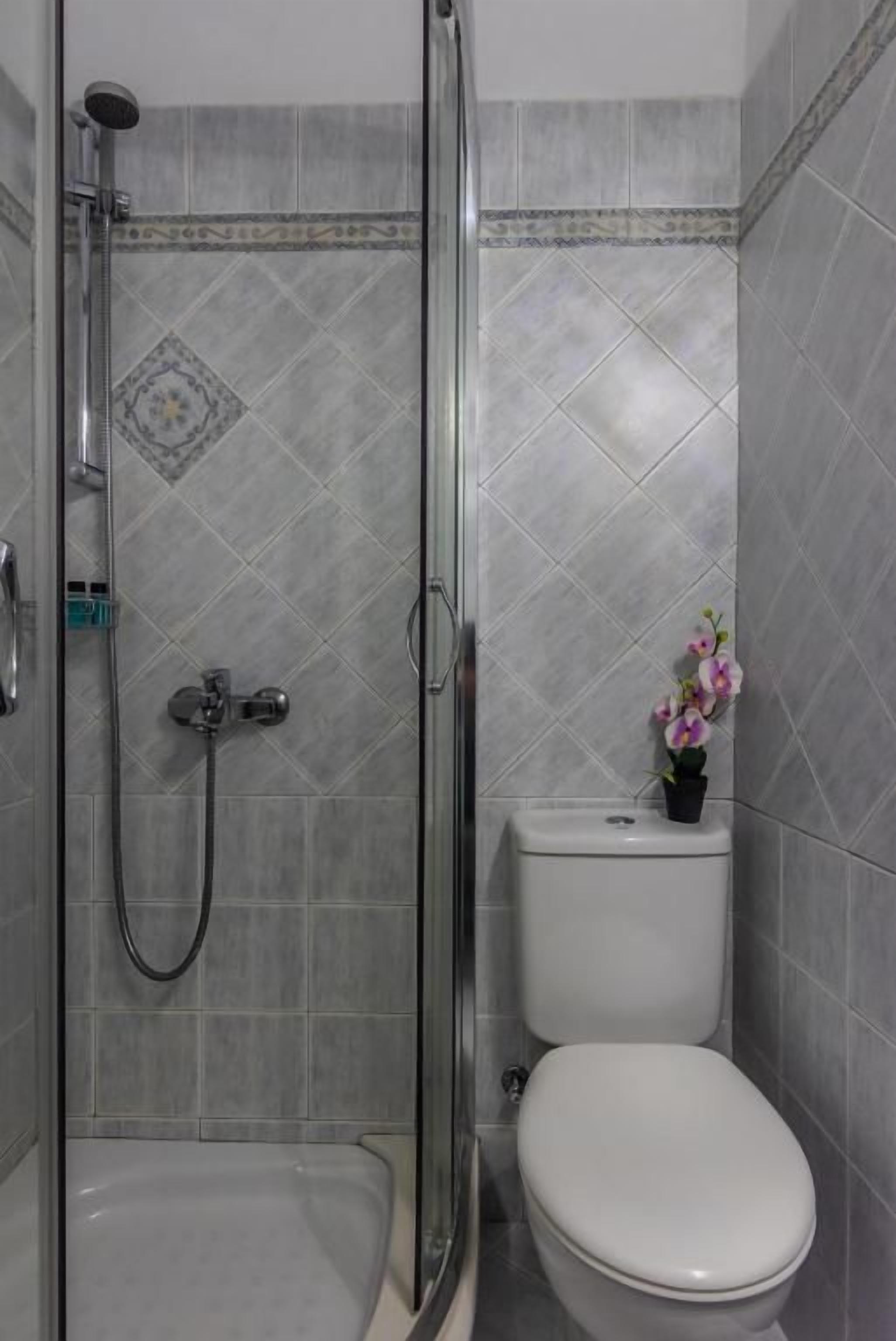 A bathroom with a shower, toilet, and a small flower arrangement.