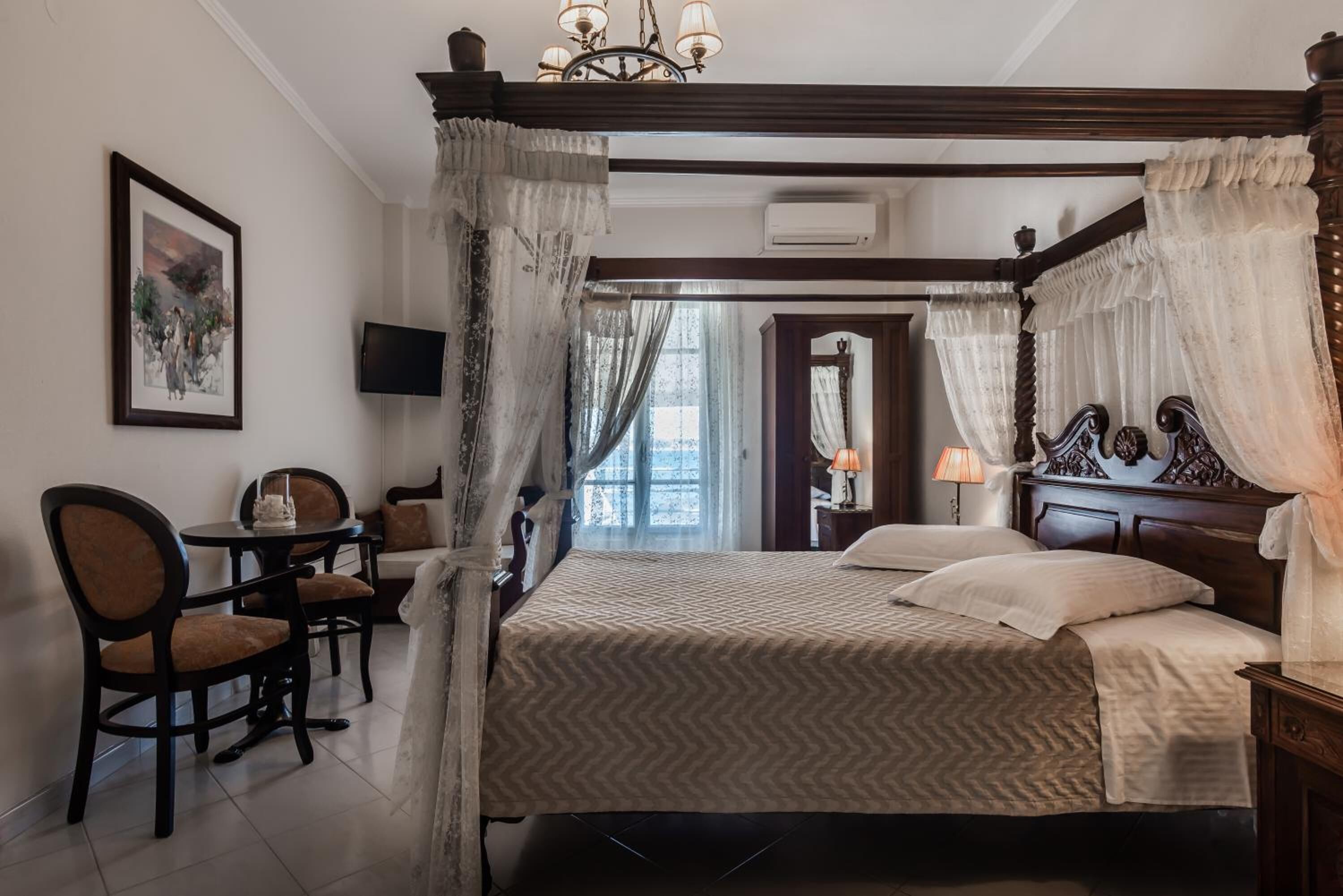 A bedroom with a four-poster bed, a desk with chairs, a television, and a painting on the wall.