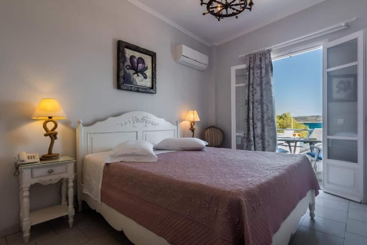 A bedroom with a bed, two bedside tables with lamps, a wall-mounted air conditioner, and a large window with a view of the outside.