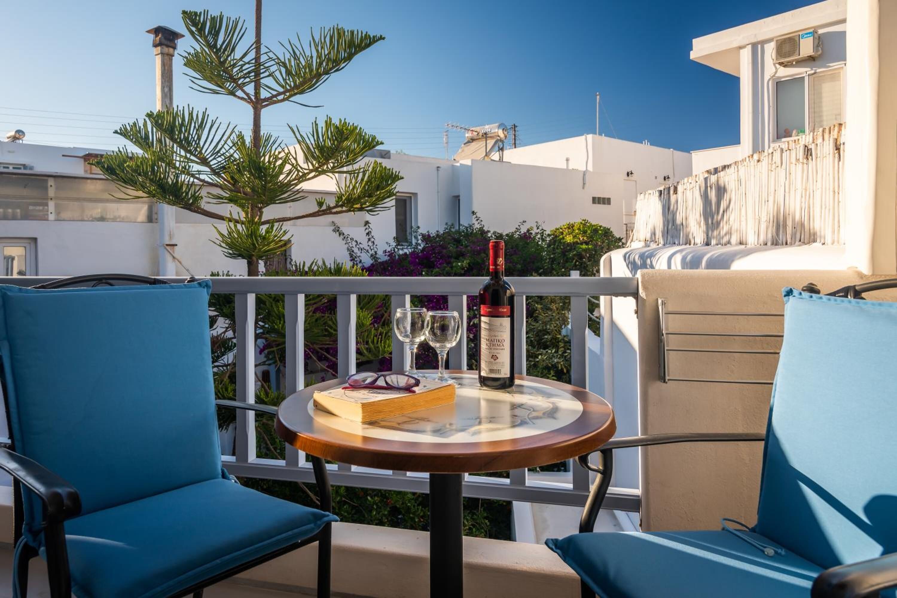 A balcony with a table set for two, featuring a bottle of wine, two glasses, and a book.