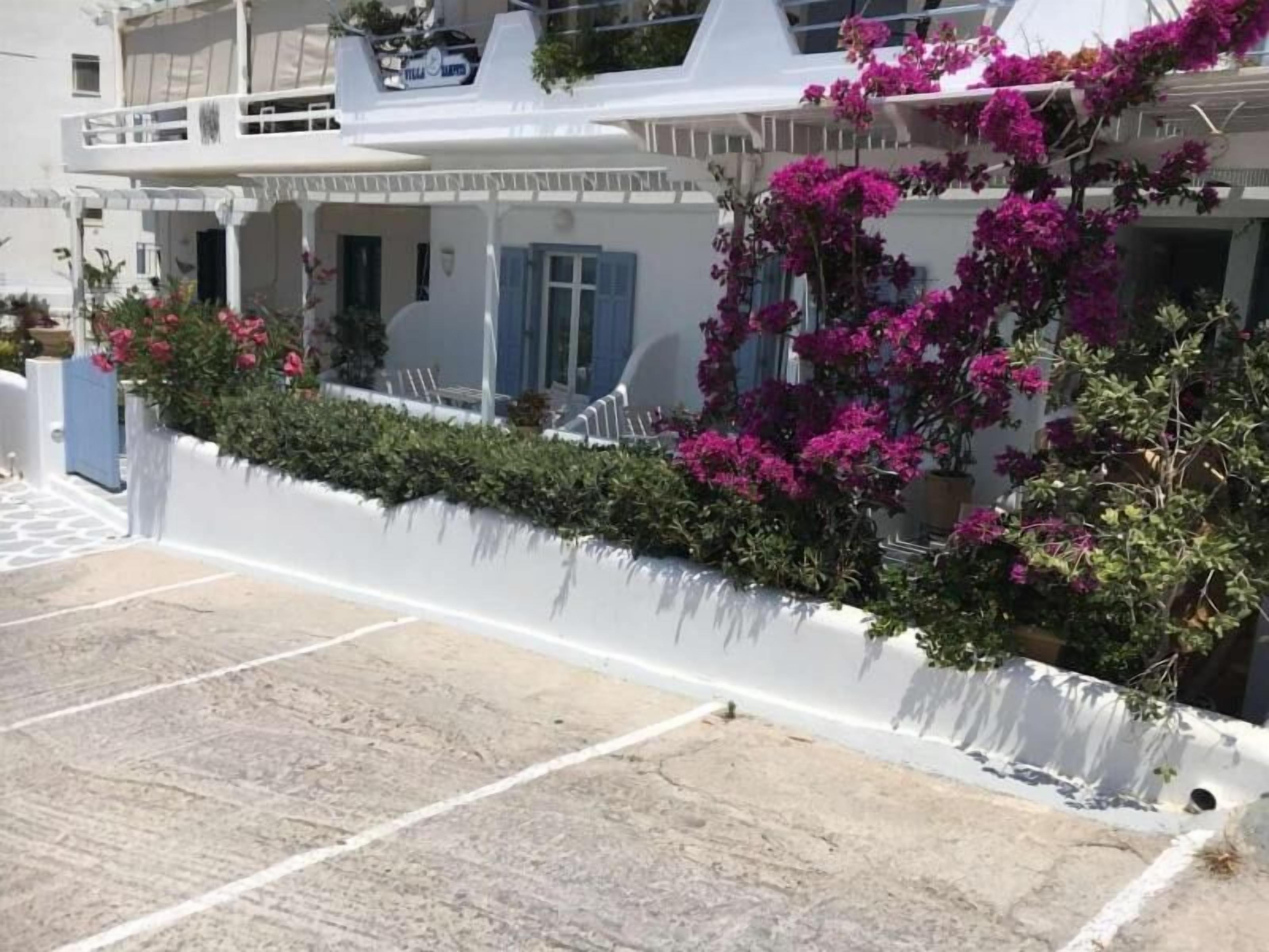 Un edificio blanco con un balcón, un área de estar al aire libre techada y coloridas flores de buganvilla rosa.