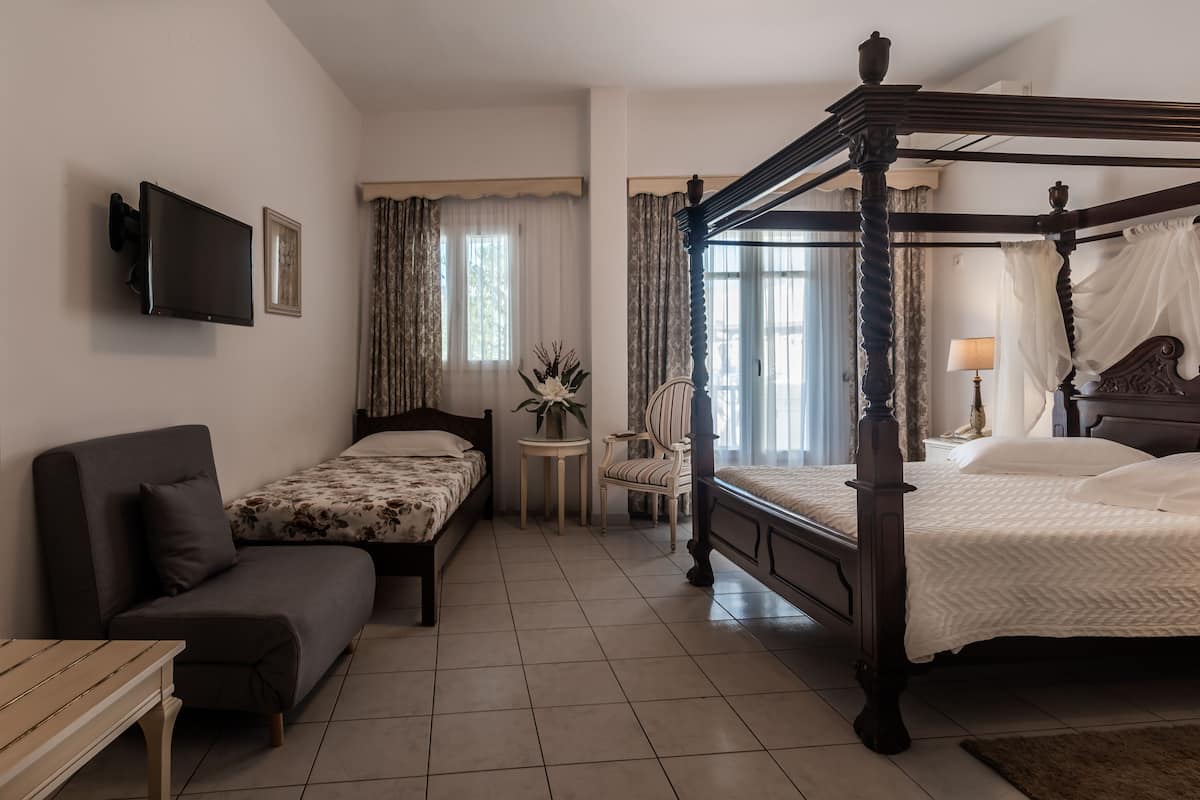 A bedroom with a four-poster bed, a sofa, a small table, and a TV mounted on the wall.