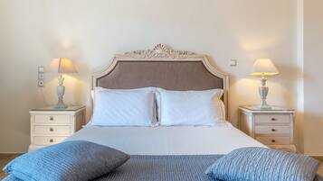 A neatly made bed with white linens and two blue pillows, flanked by two bedside tables with lamps.