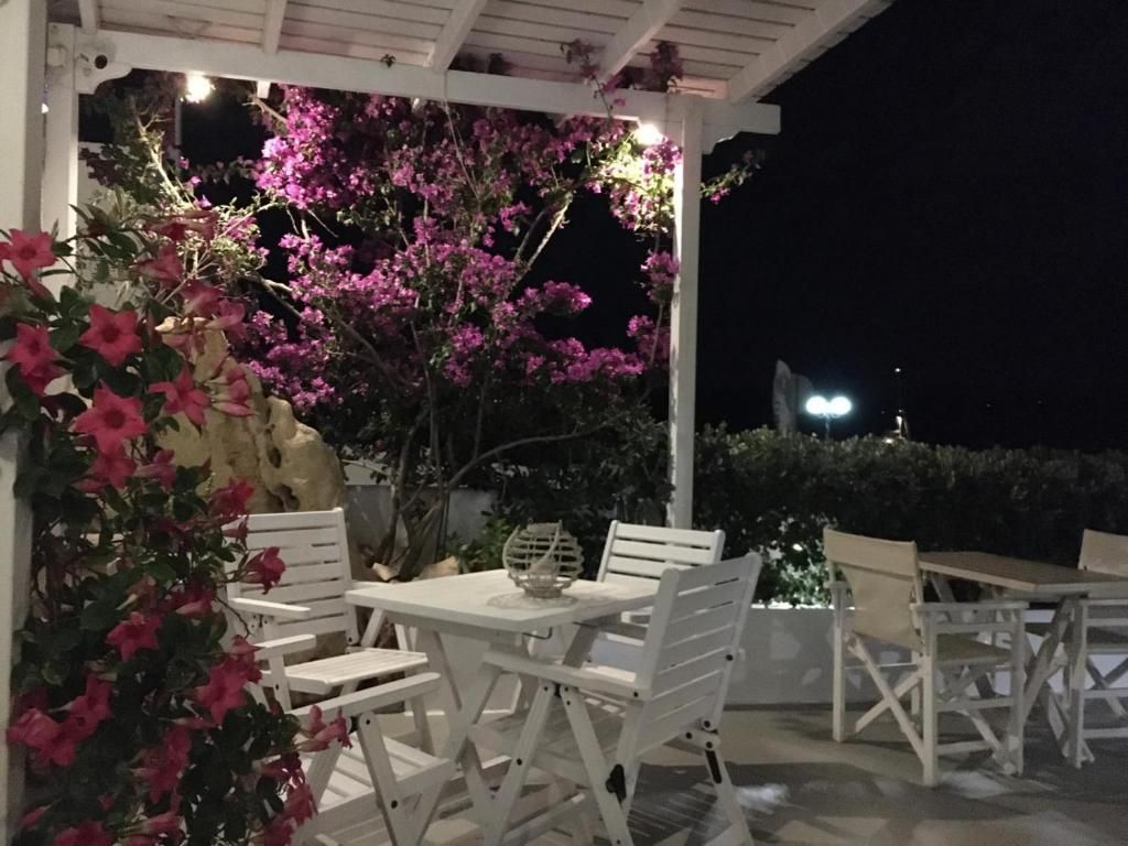 An outdoor patio with white furniture, including a table and chairs, surrounded by pink flowering plants.