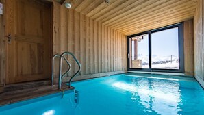 Une piscine intérieure aux murs en bois, offrant une vue sur des montagnes enneigées.