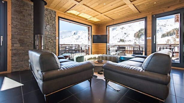 Un intérieur moderne avec des canapés en cuir, un mur en pierre, de grandes fenêtres et une cheminée.