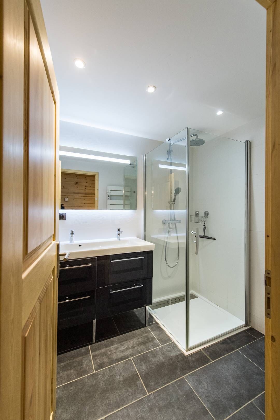 Une salle de bain moderne avec une douche à paroi de verre, un meuble-lavabo à deux vasques et une porte en bois.