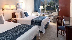Ein Hotelzimmer mit zwei Betten, einem Schreibtisch, Stühlen und Blick auf einen Balkon mit Geländer.