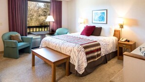 Ein Hotelzimmer mit einem Bett, zwei Stühlen, einer Bank, einem Schreibtisch und einem Fenster mit Vorhängen.