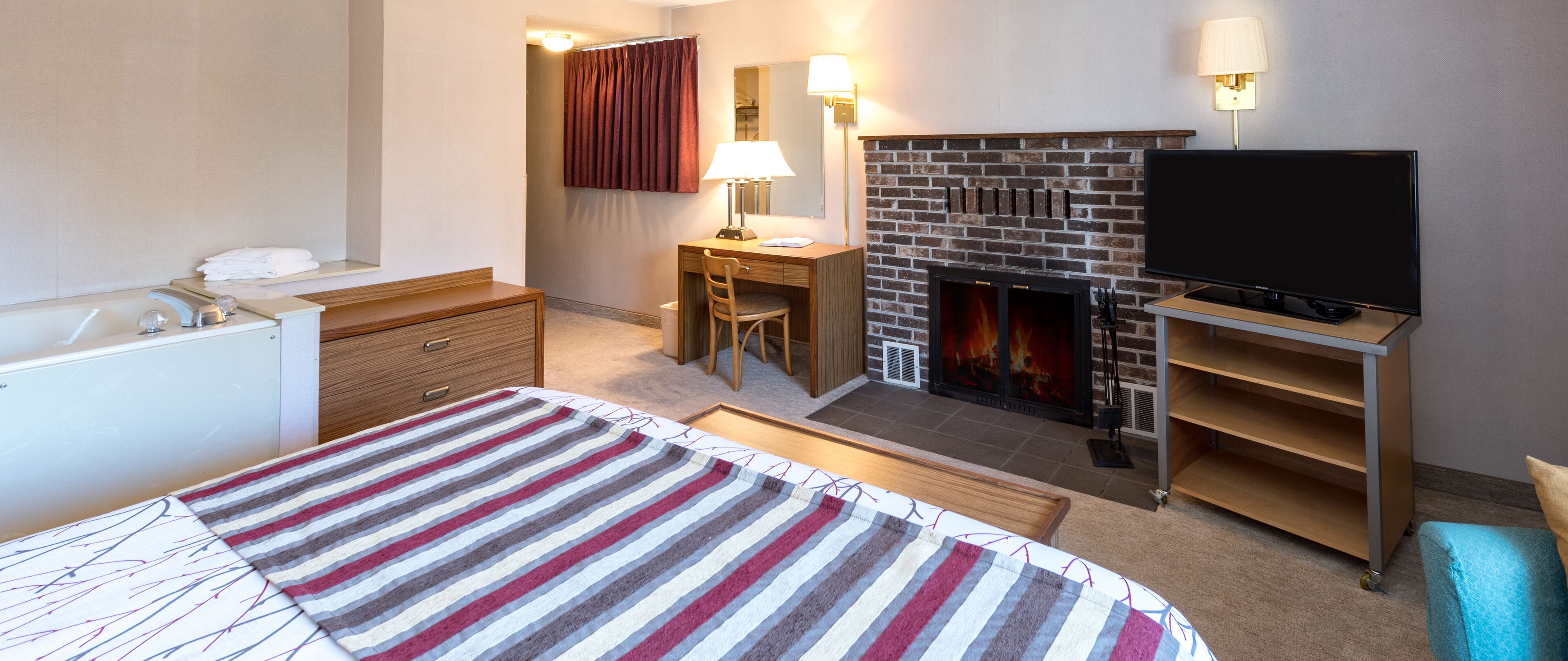 Una habitación de hotel con cama, escritorio, televisor, chimenea y baño.