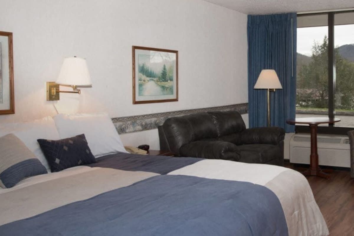 A hotel room with a bed, a leather chair, a table, and a large window with a mountain view.