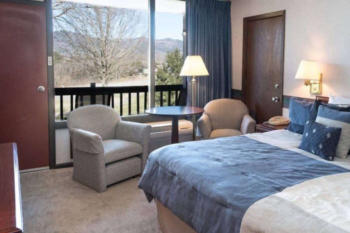 Habitación de hotel con cama, dos sillones, una mesita, escritorio, televisor y vistas al exterior.