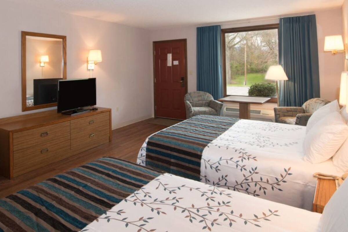 Habitación de hotel con dos camas, un televisor sobre un tocador de madera, un escritorio y una ventana con cortinas.