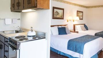 A kitchen with a stove and sink, and two adjacent beds with headboards and pillows.