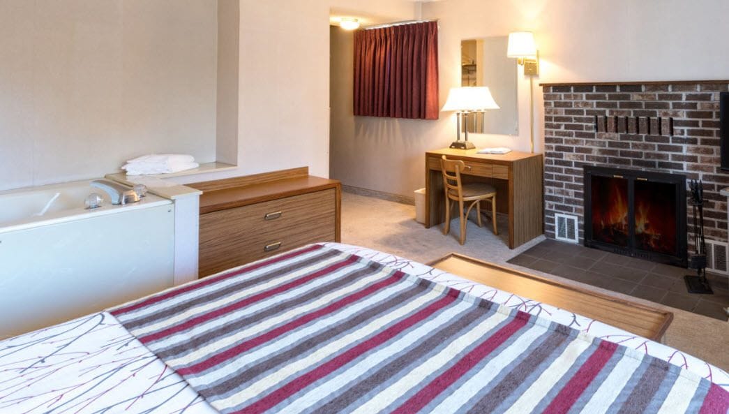 A hotel room with a bed, a desk, a chair, a fireplace, and a bathroom.