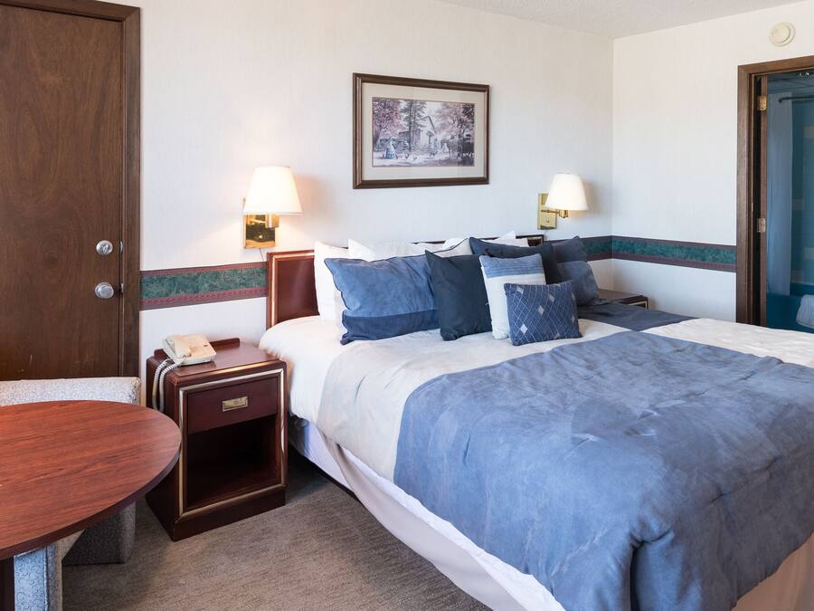 A hotel room with a bed, bedside lamps, a desk, and a chair.