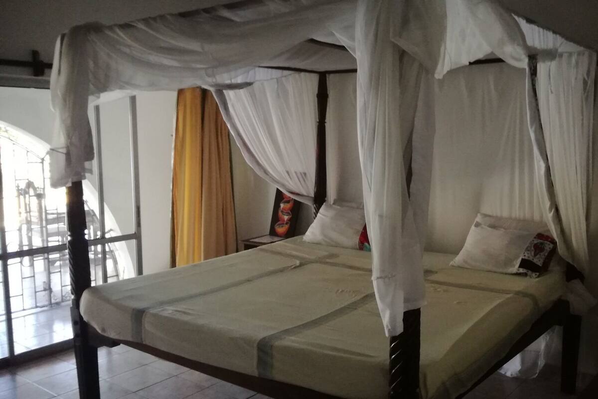 Un lit à baldaquin, une fenêtre avec des rideaux et un oreiller à motifs floraux.