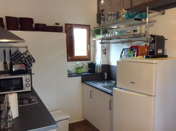 A compact kitchen with a microwave, toaster, and refrigerator. There are shelves above the counter holding various kitchen items.