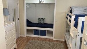 A bedroom with a bunk bed, a dresser, a closet, and a small seating area with a pillow and a blanket. - Cozy home, quiet neighborhood, near OOB attractions! (Old Orchard Beach)