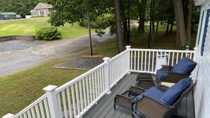 A covered deck with white railings, wicker furniture, and a view of a residential street. - Cozy home, quiet neighborhood, near OOB attractions! (Old Orchard Beach)