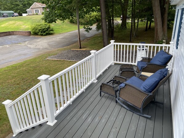 A covered deck with white railings, wicker furniture, and a view of a residential street.