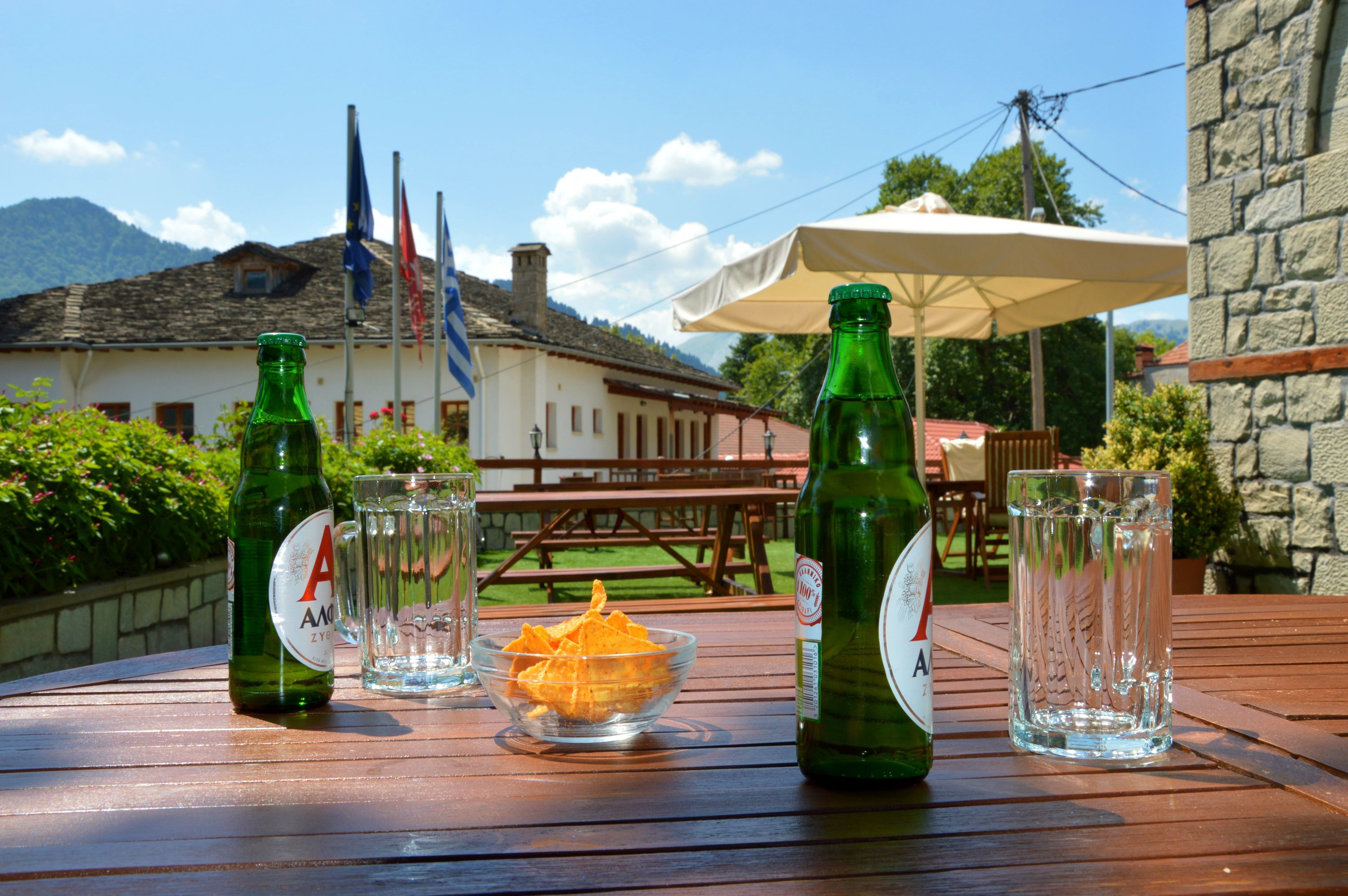 A wooden table with two green bottles, a glass, and a bowl of snacks.