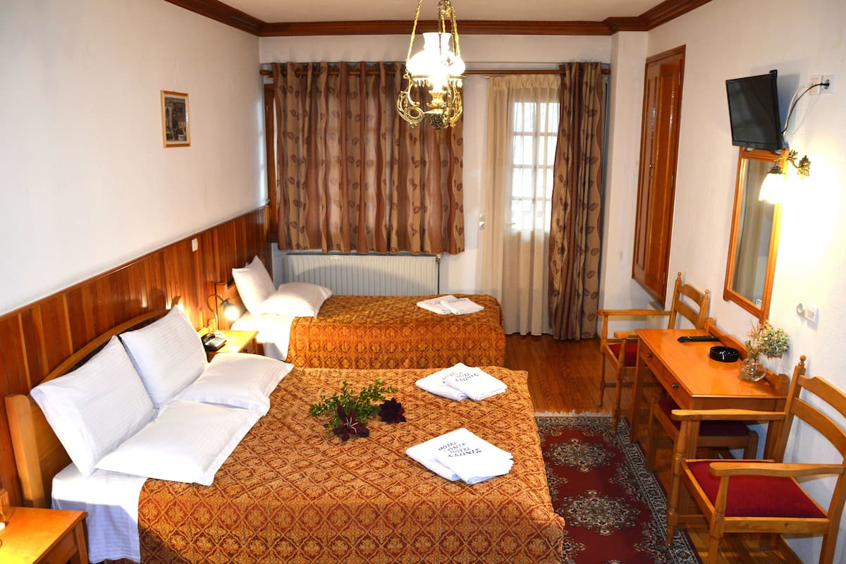 Une chambre d’hôtel avec deux lits, une tête de lit en bois, une table à manger avec des chaises, un téléviseur et une fenêtre avec des rideaux.
