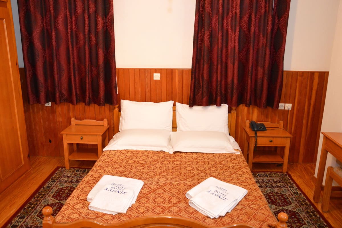Une chambre d’hôtel avec une tête de lit en bois, un lit avec du linge de lit blanc, deux tables de chevet, un téléphone et une petite table de nuit en bois.