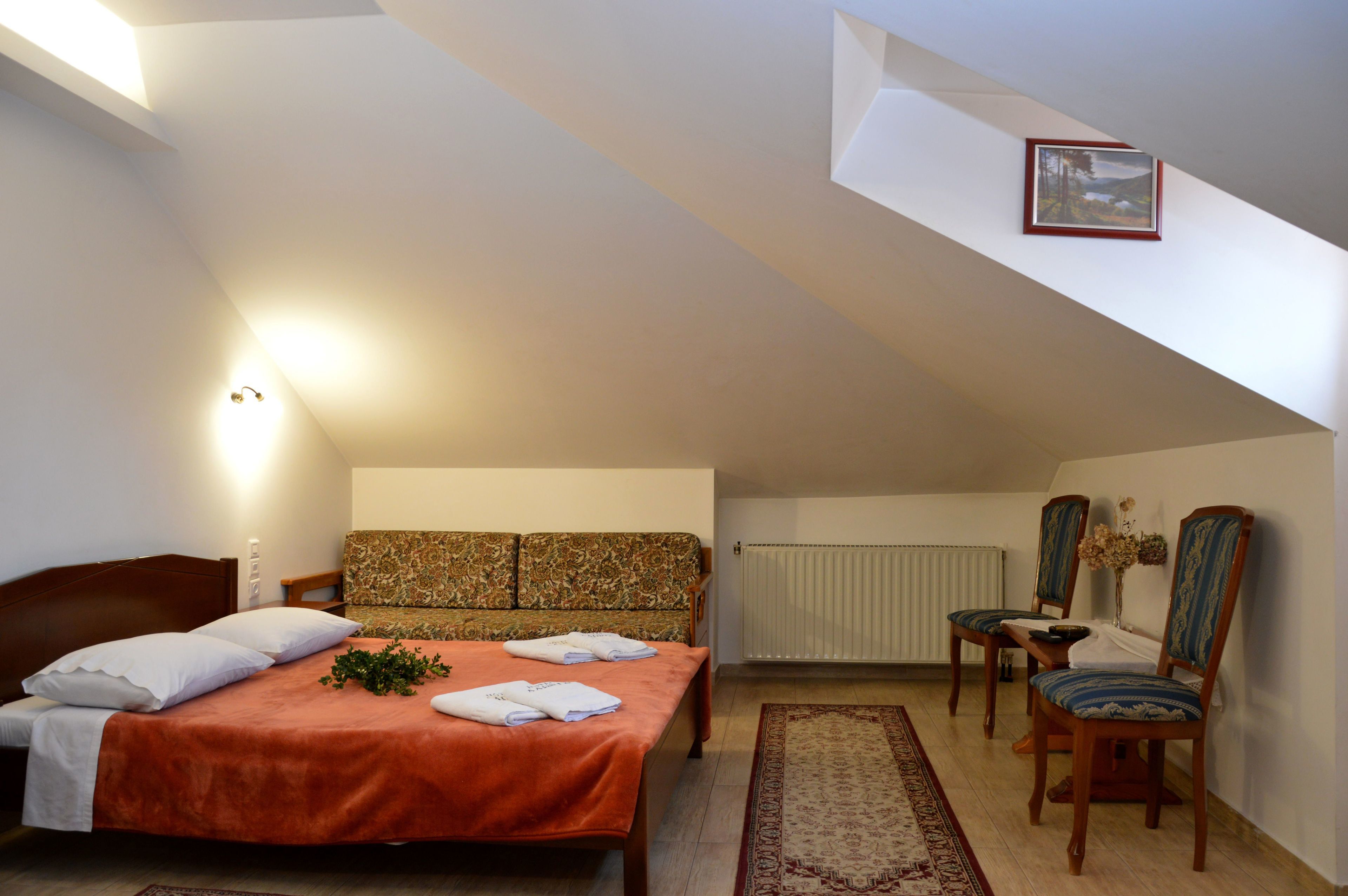 A bedroom with a bed, a sofa, two chairs, a table, and a picture on the wall.