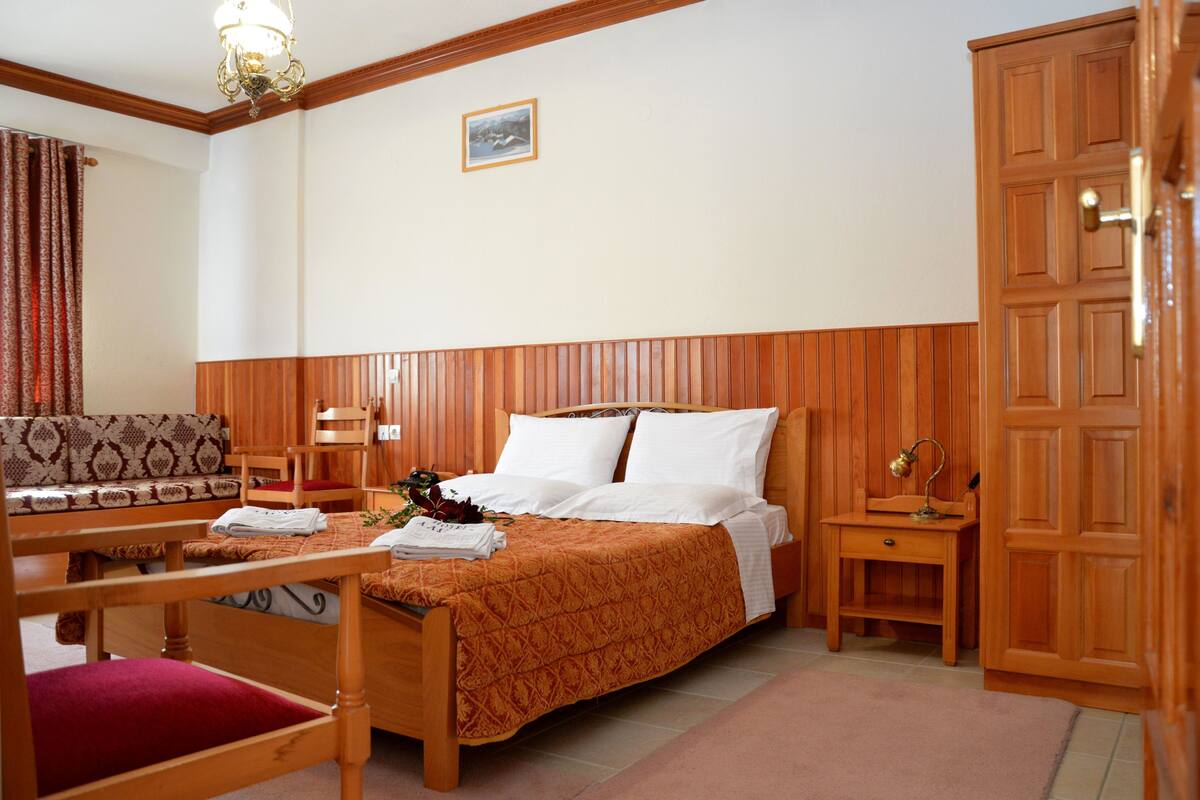 Une chambre d’hôtel avec un lit en bois, une table de chevet en bois, une chaise, un bureau et une armoire.