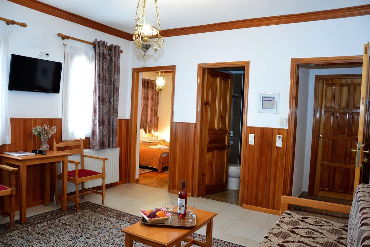 Un salon chaleureux avec un plancher en bois, une table à manger avec des chaises, un téléviseur fixé au mur et une porte donnant sur une chambre.