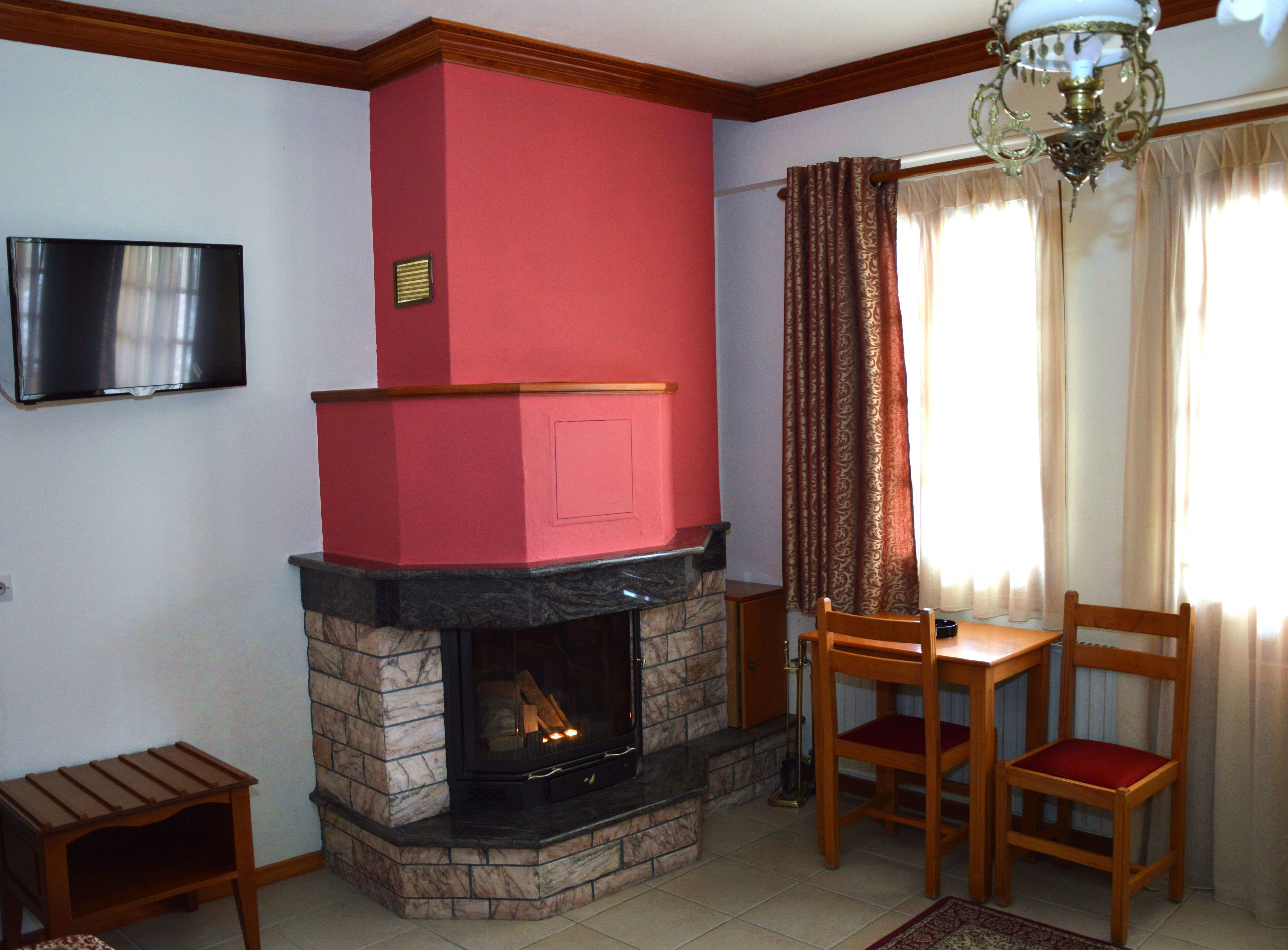 A living room with a fireplace, a television mounted on the wall, and a dining area with two wooden chairs.