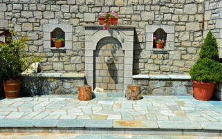 Un muro de piedra con un arco central, flanqueado por dos ventanas pequeñas. Hay plantas en macetas en los alféizares de las ventanas y un árbol pequeño a la derecha.