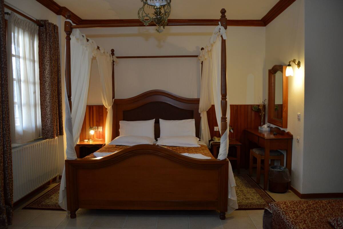 Un lit à baldaquin avec une tête de lit en bois, une table de chevet avec une lampe, un miroir et une petite chaise en bois.