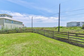 A grassy area with a wooden fence, utility poles, and two buildings in the background. - You can truly enjoy the Port A lifestyle in this colorful home. Monthly rentals (Port Aransas)