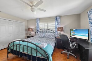 A bedroom with a bed, a desk, a chair, a television, and a ceiling fan.
