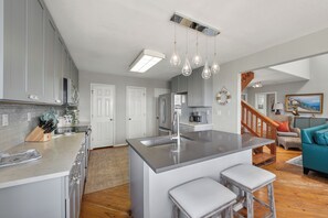 A modern kitchen with a central island, pendant lighting, and a view into the living area. - You can truly enjoy the Port A lifestyle in this colorful home. Monthly rentals (Port Aransas)