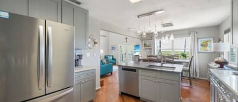 A modern kitchen with stainless steel appliances, a central island, and a view to the living area.