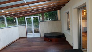 Un espacio al aire libre cubierto con terraza de madera, un jacuzzi y un ventanal corredizo que da a una habitación.